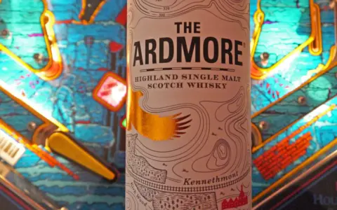 Flasche "The Ardmore" Highland Single Malt Scotch Whisky steht vor einem bunten Flipperautomaten. Ein spannender Ardmore Whisky Test!