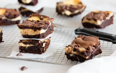 Schokoladige cheesecake brownies mit cremiger Füllung und Schokostückchen, gestapelt auf einem Gitter.