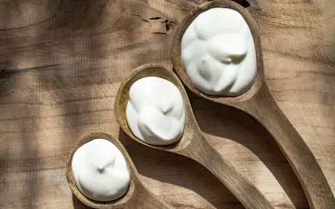 Tre cucchiai di legno pieni di panna da cucina su un tagliere rustico.