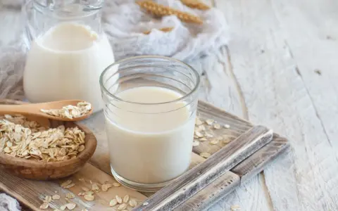 Szklanka i dzbanek z mlekiem owsianym, obok miseczka płatków owsianych. Idealne na zdrowe śniadanie, mleko 2 procent kcal.