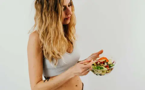 Donna con capelli biondi mangia un'insalata fresca, parte della sua vlckd dieta.