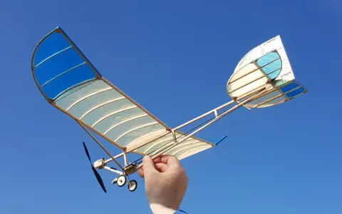 Ein handgefertigtes Modellflugzeug mit blau-weißen Flügeln, gehalten von einer Hand, bereit zum Flug. Ein echter slow flyer.