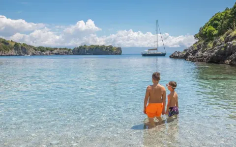Due bambini esplorano le acque cristalline del Cilento, tra le sue spiagge perfette per famiglie. Una barca a vela all'orizzonte completa il quadro idilliaco.