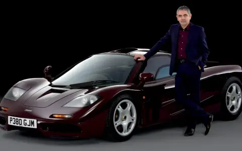Rowan Atkinson w garniturze opiera się o swój bordowy McLaren F1. To jeden z jego ulubionych samochodów.