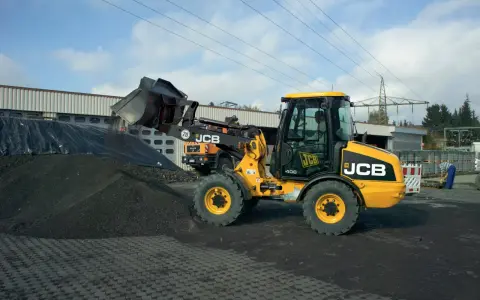 Żółta ładowarka JCB 406 z podniesioną łyżką, gotowa do pracy. Dane techniczne tej maszyny pozwalają na efektywne przenoszenie materiałów.