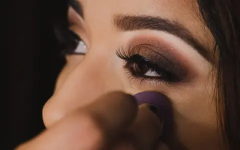 Un œil maquillé avec un smoky eyes facile, rehaussé de paillettes. Une éponge violette est utilisée pour estomper le fond de teint.