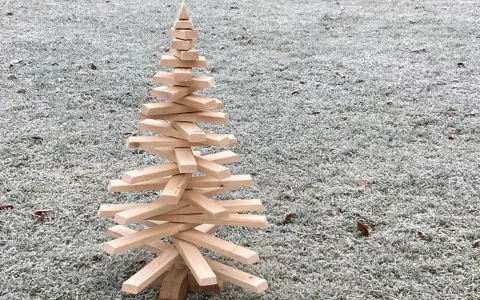 Ein selbstgemachter Tannenbaum aus Holz, der auf frostigem Gras steht. Eine rustikale Deko-Idee, um den Winter zu begrüßen.