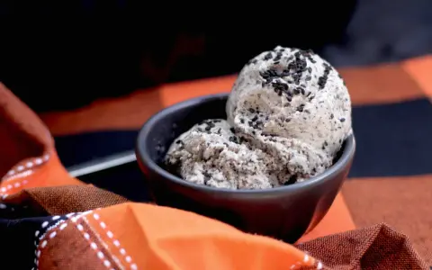 Zwei Kugeln cremiges **black sesame ice cream** in einer Schale, bestreut mit schwarzen Sesamsamen, auf einem karierten Stoff.