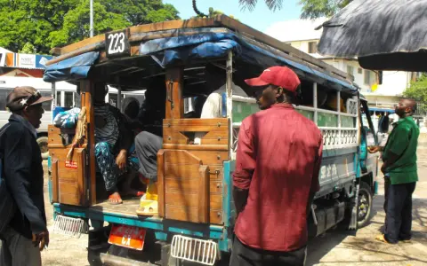 Ludzie wsiadają do dala dala na Zanzibarze. Widać drewnianą konstrukcję pojazdu i pasażerów.