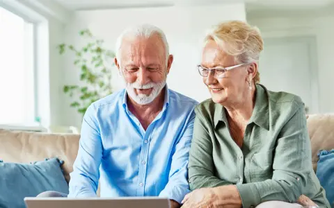 Uśmiechnięta para seniorów przegląda w internecie informacje, jak załatwiać sanatorium.