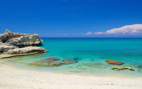 Spiaggia di Santa Domenica con rocce bianche e mare cristallino sotto un cielo azzurro.