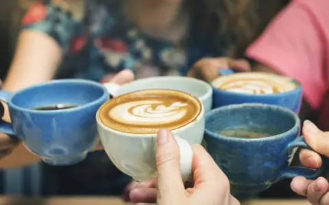 Vier Hände halten bunte Kaffeetassen. Der Kaffee reizt die Blase, aber der Genuss ist es wert.