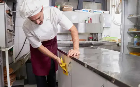 Cocinero con delantal limpiando encimera de acero inoxidable. Esencial para la limpieza de restaurantes.