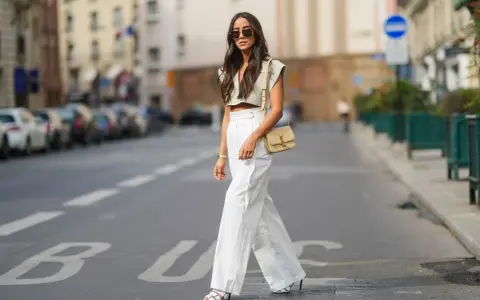 Stilvolle Dame in Paris, die eine weiße Leinenhose kombiniert mit einem kurzen Top und einer Umhängetasche trägt.