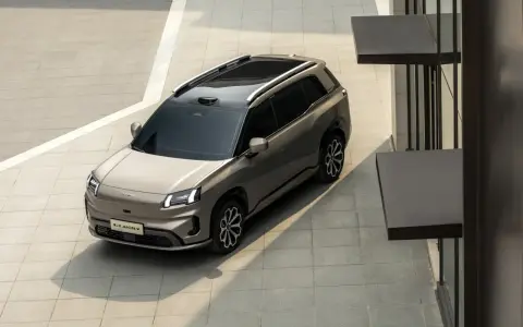 Szary elektryczny SUV GAC Aion V z czarnym dachem i relingami, zaparkowany na zewnątrz.