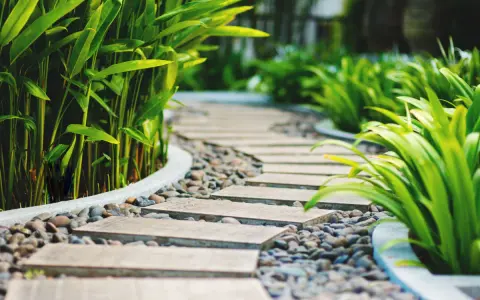 Un moderno camminamento giardino con lastre in pietra e ghiaia, circondato da rigogliosa vegetazione verde.