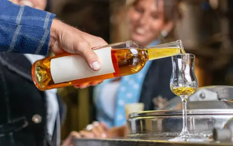 Mężczyzna nalewa złocisty grappa alkohol do kieliszka. W tle uśmiechnięta kobieta.