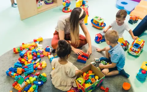Dzieci bawią się klockami z opiekunką, co może być możliwe dzięki dofinansowaniu do żłobka. Radość i nauka przez zabawę.