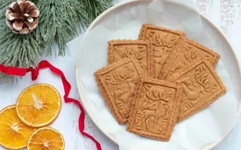 Assiette de sablés rennes de Noël, décorée de branches de sapin givrées, de ruban rouge et de tranches d'orange séchée.