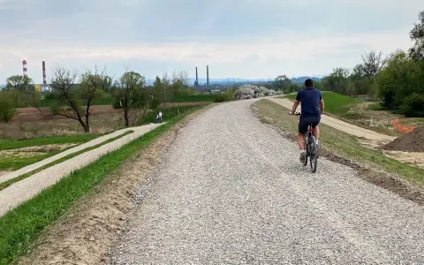 Mężczyzna na rowerze przemierza nową ścieżkę rowerową w Skawinie. W tle widać przemysłowe kominy i zielone tereny.