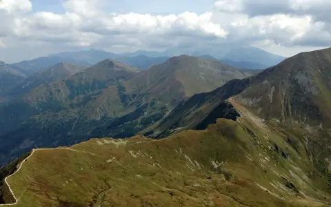 Widok na pasmo górskie, gdzie w Tatry prowadzi wydeptana ścieżka. Chmury na niebie.