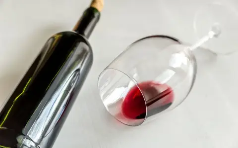 Ciemna butelka i przewrócony kieliszek z czerwonym winem. Idealny wieczór z winem półwytrawnym.