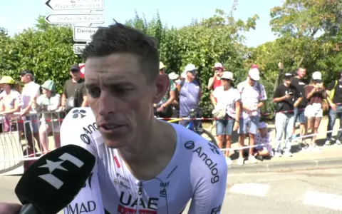 Brandon McNulty, Radfahrer im UAE-Trikot, gibt ein Interview. Im Hintergrund stehen Zuschauer und Straßenschilder.