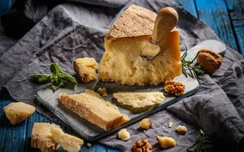 Kawałek parmezanu z nożem, okruchy sera, orzechy i bazylia. Czy parmezan można mrozić? Tak, można go mrozić, choć może stracić nieco na konsystencji.