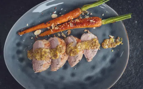 Zarte Scheiben von **schweinefilet grillen** mit Honig-Senf-Sauce und karamellisierten Karotten, bestreut mit Mandelsplittern.