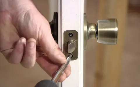 Mano usando un destornillador para desmontar una cerradura de puerta interior, quitando los tornillos de la placa.