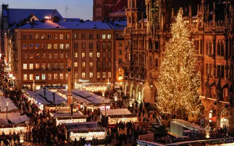 A bustling Christmas market in Munich, Germany, with a towering, illuminated tree and snow-dusted stalls.
