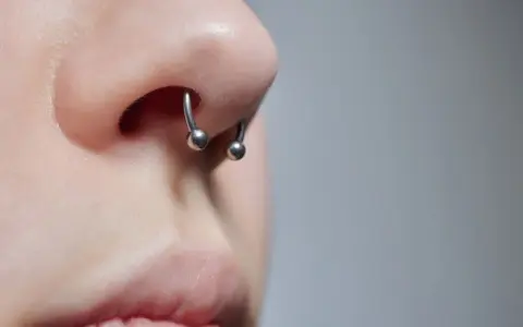 Zbliżenie na nos z kolczykiem typu septril piercing. Metalowy okrąg z dwoma kulkami subtelnie zdobi przegrodę nosową.