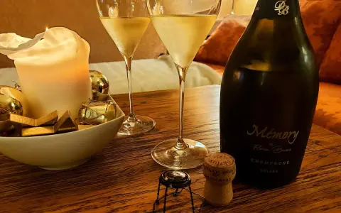 Zwei Gläser Champagner, eine Kerze und eine Flasche "Memory" auf einem Holztisch. Der Champagnergehalt ist hierbei nicht ersichtlich, aber die Stimmung ist festlich.
