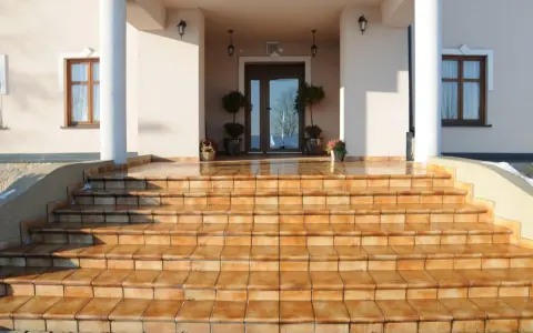 Amplias escaleras exteriores para casas de dos pisos, con escalones de baldosas naranjas que conducen a una entrada principal.