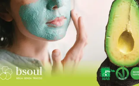 Donna con maschera viso fai da te verde, accanto ad avocado. Certificazioni bio e vegan.
