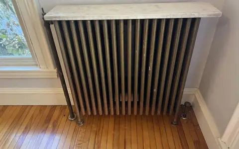 Radiador de latón con tapa de mármol, un ejemplo de calefacción antigua, junto a una ventana.