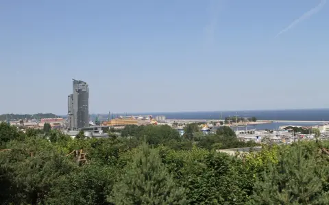 Widok na port w Gdyni z dominującym wieżowcem. W oddali morze, a na pierwszym planie zieleń drzew. Kamienna Góra w Gdyni oferuje takie panoramy.