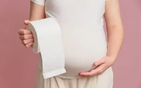 Ciężarna kobieta trzymająca rolkę papieru toaletowego, symbolizująca luźne stolce w ciąży w 1 trymestrze.