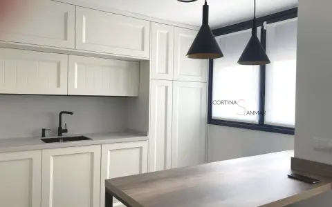 Cocina moderna con armarios blancos, encimera gris, grifo negro y cortinas blancas. Ideas para tu cocina.