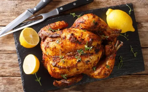 Pollo al horno dorado y jugoso, adornado con tomillo fresco y acompañado de limones cortados. Un festín listo para servir.