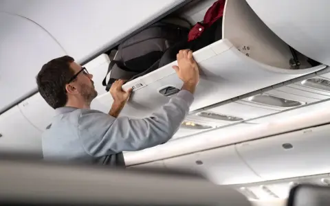 Man stänger bagagehyllan med handbagage ombord på ett flygplan från Austrian Airlines.