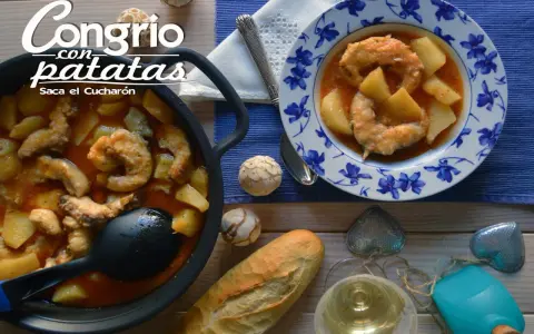 Congrio con patatas, un plato reconfortante servido en cazuela y plato decorado. Acompañado de pan y vino blanco.