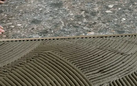 Pose de mortier pour un double encollage de carrelage. Les mains d'un carreleur préparent la surface.