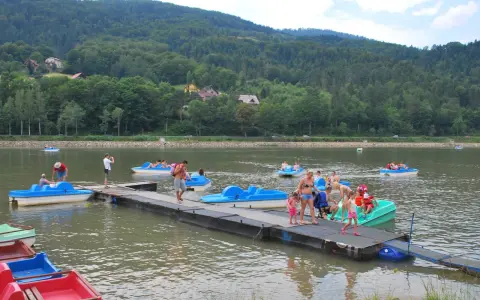 Wakacyjny dzień na Jeziorze Żywieckim. Ludzie pływają na rowerach wodnych, czując się jak na karaibskiej plaży.