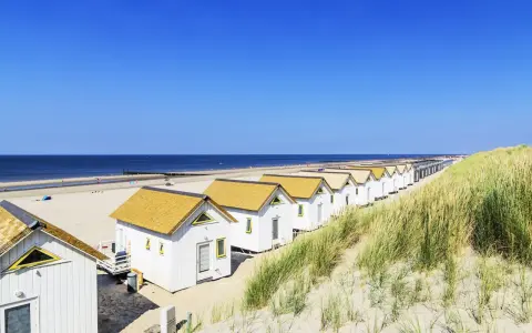 Reihen von weißen Strandhäusern mit gelben Dächern am **Holland Strand** unter blauem Himmel.