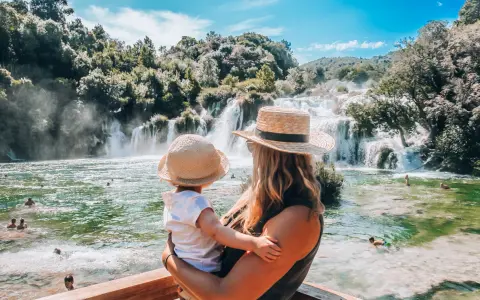 Mama z dzieckiem podziwia wodospady w parku Krka w Chorwacji. Woda jest krystalicznie czysta, a wokół bujna zieleń.