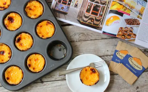 Pyszne, lekko przypieczone pastel de nata w blaszce i na talerzyku. Obok magazyn z widokiem na Lizbonę i tramwaje.