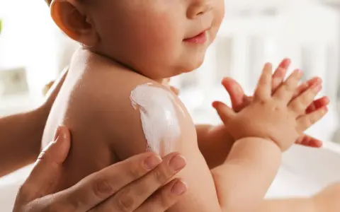 Delikatna pielęgnacja noworodka. Kremowanie ramienia dziecka, które ma lekko łuszcząca się skórę.
