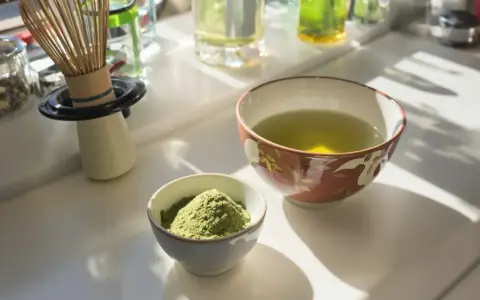 Zwei Schalen auf einem Tisch: eine mit grünem Pulver, die andere mit aufgebrühtem Sencha Tee. Die Wirkung von Sencha Tee ist belebend.
