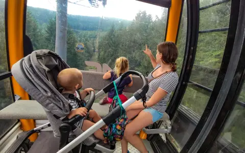 Rodzina w kolejce gondolowej w Górach Izerskich, Świeradów-Zdrój. Dzieci zachwycone widokiem lasu i innych wagoników.